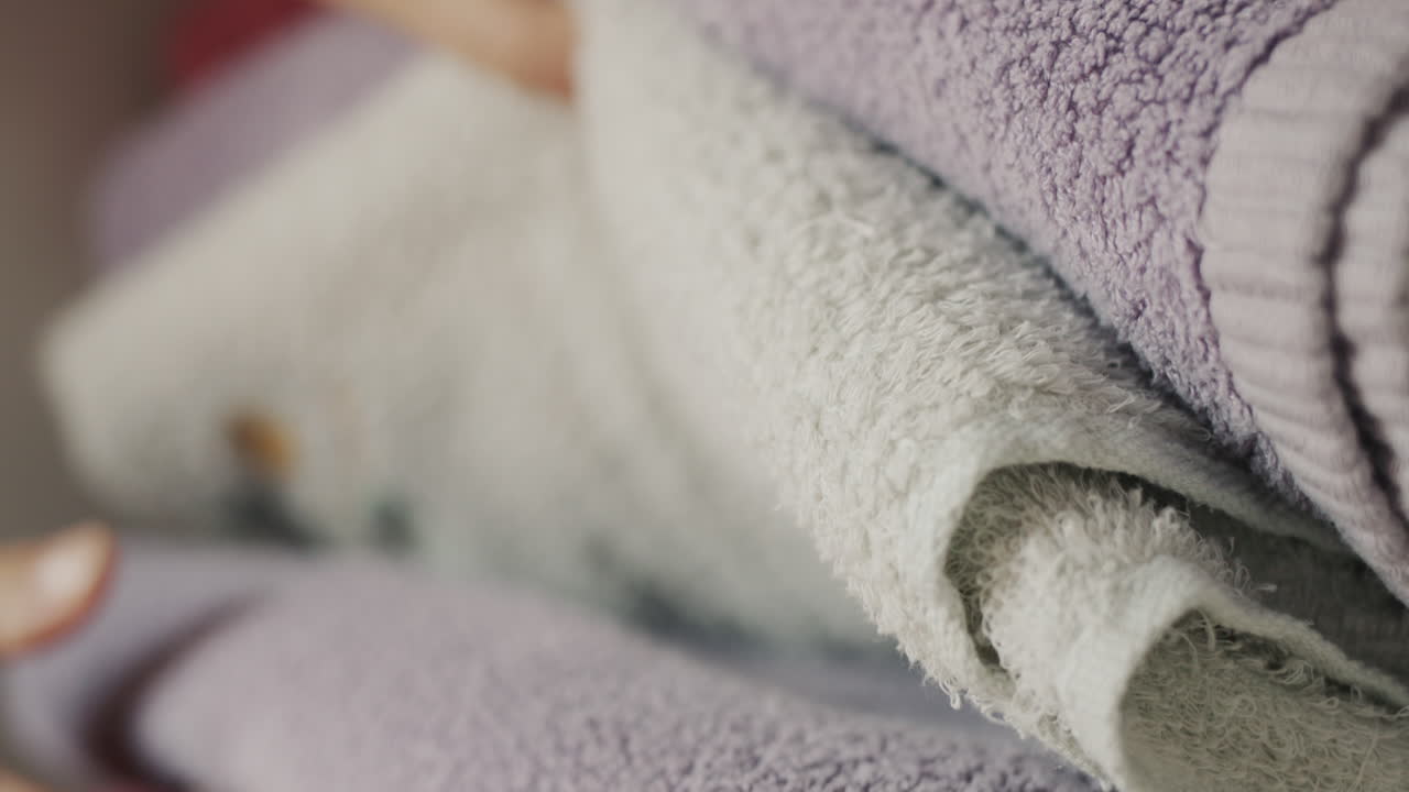 Women's fingers sort through clean towels on a shelf in the closet