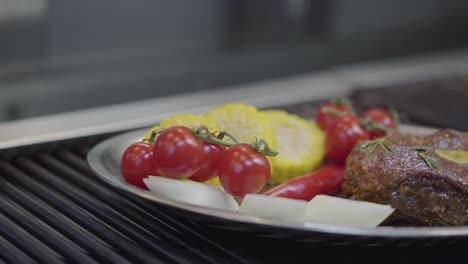 the plate with the meat, corn, cherry tomatoes, lemongrass and chili pepper lying on the grill close up.