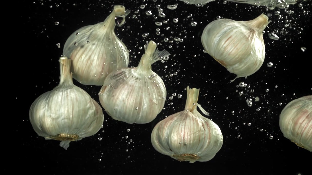 Bulbi d'aglio freschi che galleggiano nell'acqua con bolle