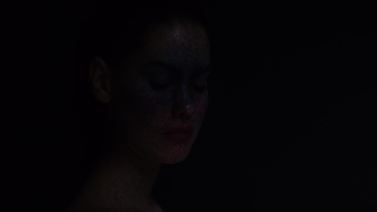 파란색 얼굴 페인트 메이크업을 입은 아름다운 여성의 초상화 매력적인 여성 공연자 창조적 표현 빛이 어두운 배경에서 사라지고 있습니다