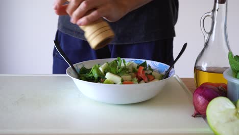 man grinding pepper on healthy salad in kitchen