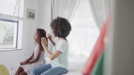 Happy-african-american-mother-and-daughter-brushing-hair-in-bedroom,-slow-motion