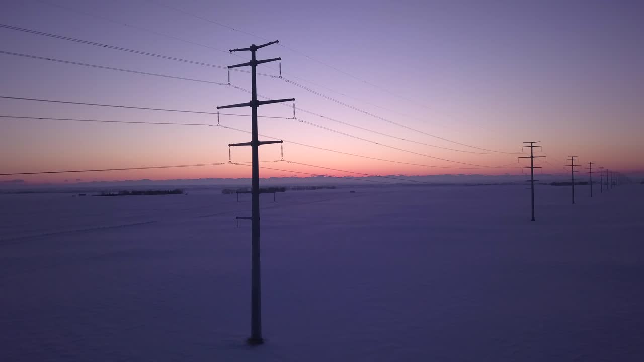Power poles with multiple wires extend to sunset horizon, aerial