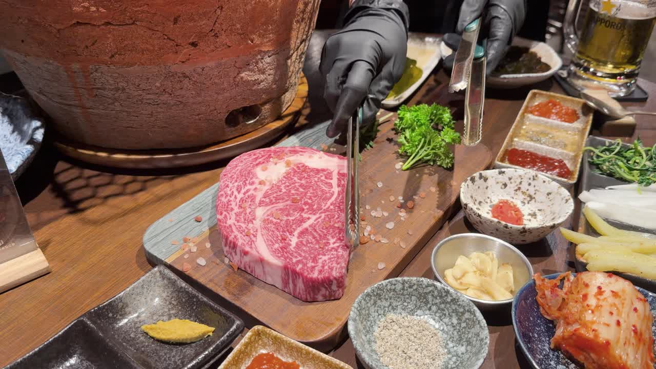 Gloved chef seasons raw wagyu steak with salt, preparing for tabletop Korean barbecue grilling