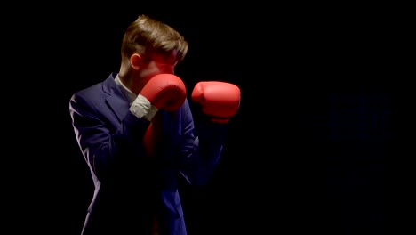 a young man in a simple blue suit and white shirt standing sideways, raises his hands with boxing gloves on combat ready, and then strikes directly