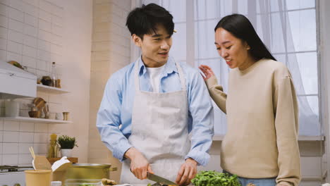 hombre japonés cortando ingredientes en la cocina, luego su amiga se acerca y habla con él