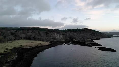 Castillo-De-Dunvegan-En-La-Isla-De-Skye,-Rodeado-De-Bosques-Y-Mar-Al-Atardecer,-Vista-Aérea