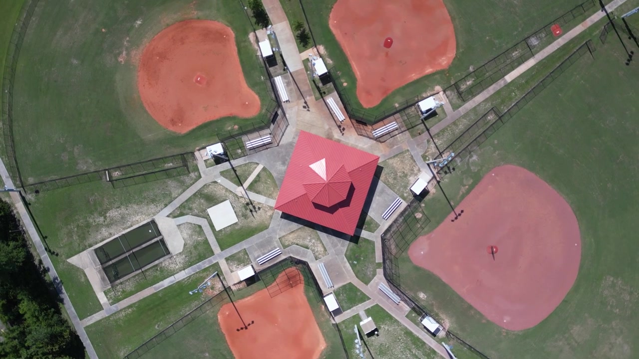 Rising spinning drone shot looking straight down at concession building between baseball fields at small sports park.