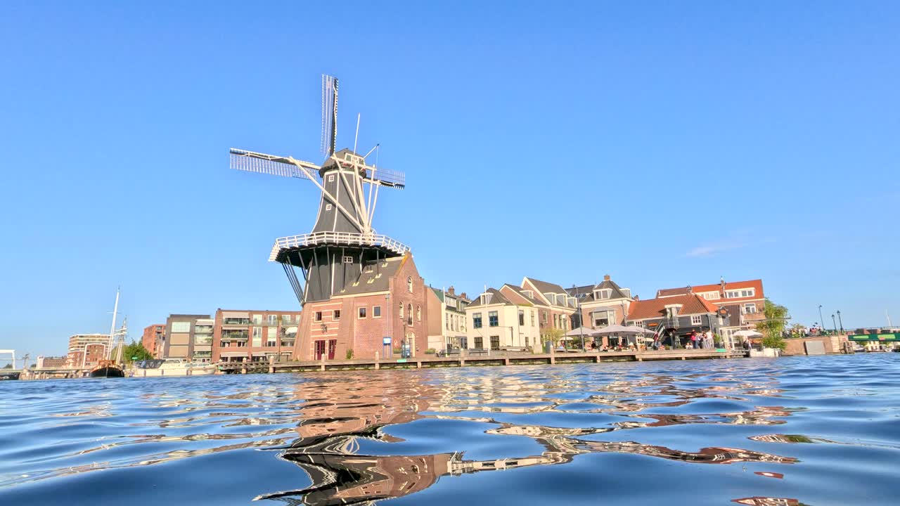 Low-angle view of windmill and buildings, bright daylight, rippling water reflection, steady camera