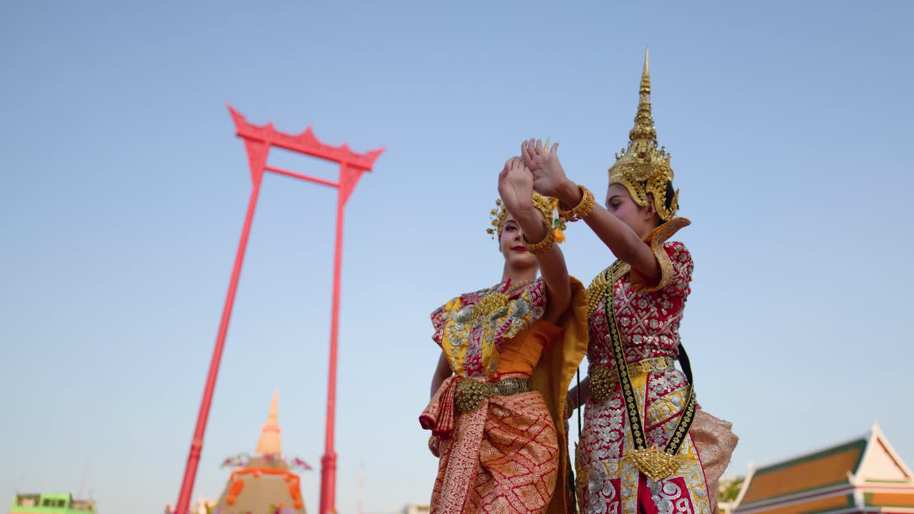 Due donne in elaborati costumi dorati eseguono la tradizionale danza thailandese Khon in un tempio.