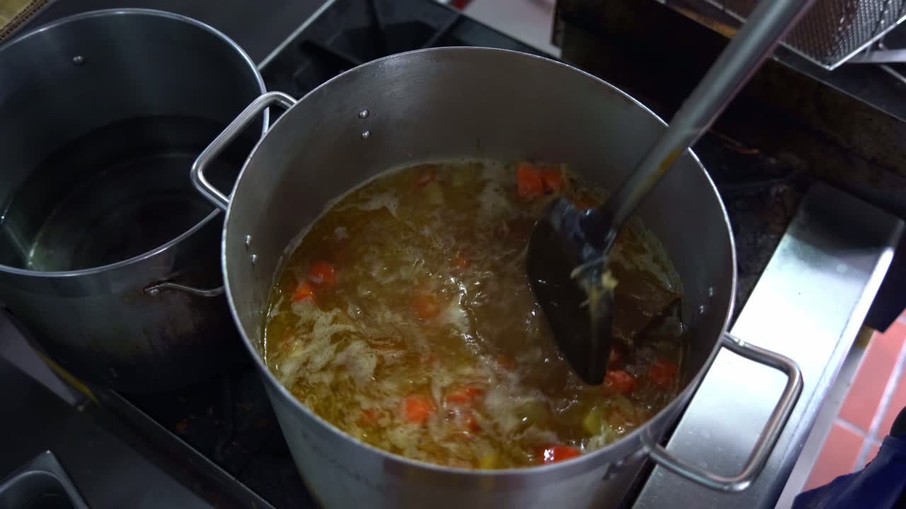 chef agregando bloques de curry roux japonés en una olla grande en la estufa, revolviendo y mezclando papas, zanahorias y cebollas, vista de arriba hacia abajo