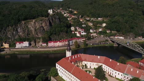 drone zoom out over the historic decin castle and colorful town by the elbe river, with lush hills in morning light