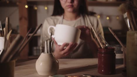 una joven alfarera examina una gran taza de té de cerámica blanca