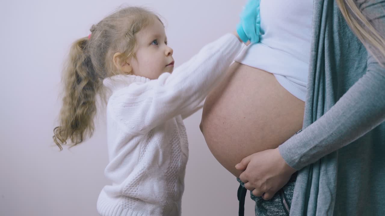 아이는 임신 한 어머니의 배와 함께 소년의 부티를 사용하여 놀고 있습니다.