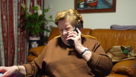 modern cheerful grandmother talking to a friend on cell phone at home