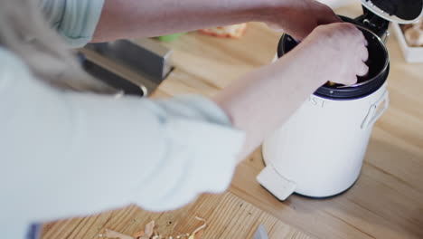 Middle-aged-caucasian-woman-putting-food-waste-in-bin-in-kitchen-at-home,-slow-motion