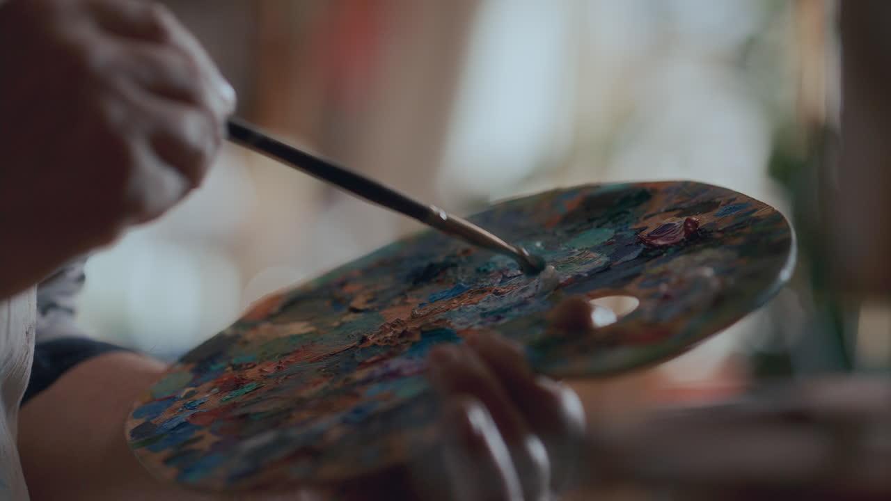 Mani di artista che mescolano colori sulla tavolozza e dipingono con il pennello.