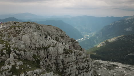 Tiro-De-Dron-De-Rombon-De-Montaña-Y-Un-Grupo-De-Excursionistas-Subiendo-Hacia-La-Cima,-Valle-En-El-Fondo,-Cielo-Nublado