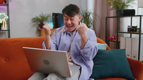 Amazed asian man use laptop computer receive good news message shocked by victory celebrate win