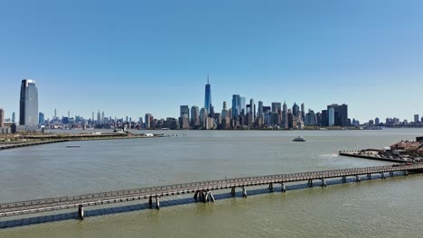 aerial flight over hudson river in new york city with beautiful skyline and one world trade center in background during sunny day with blue sky - goldman sachs tower on the left in jersey city