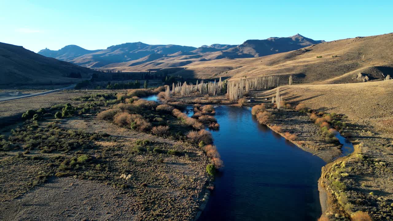 Aerial view of a blue river winding through a golden and green valley near Bariloche, Argentina, glowing in sunset light