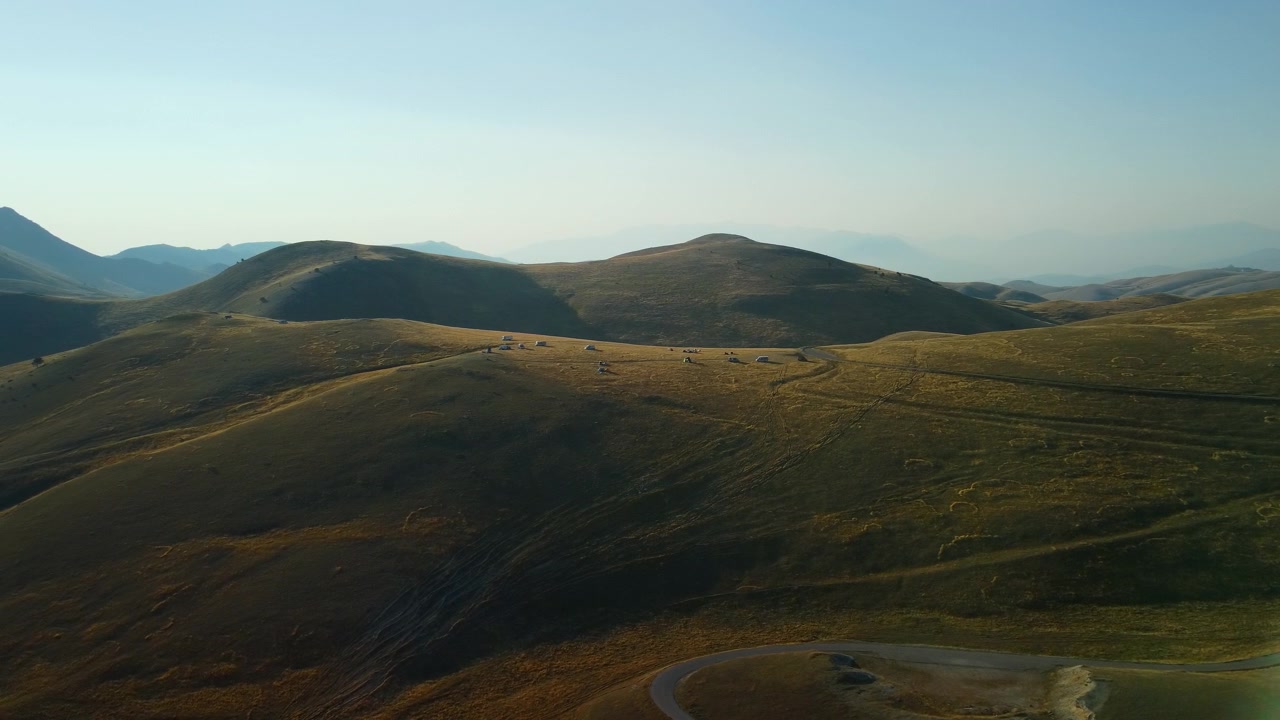 Paesaggio montano dorato ripreso da drone, panoramica aerea di terreno accidentato con camper parcheggiati sulla cresta. Destinazione di viaggio panoramica estiva