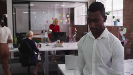 african american businessman sitting on desk in open space using tablet looking to camera