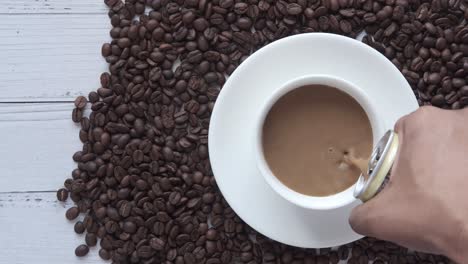 vertiendo café con leche en una taza rodeada de granos de café