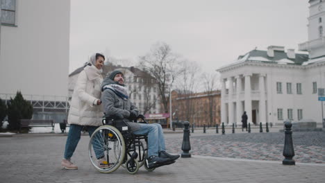 Muslimische-Frau,-Die-Ihren-Behinderten-Freund-Im-Rollstuhl-Im-Winter-Bei-Einem-Spaziergang-Durch-Die-Stadt-Mitnimmt