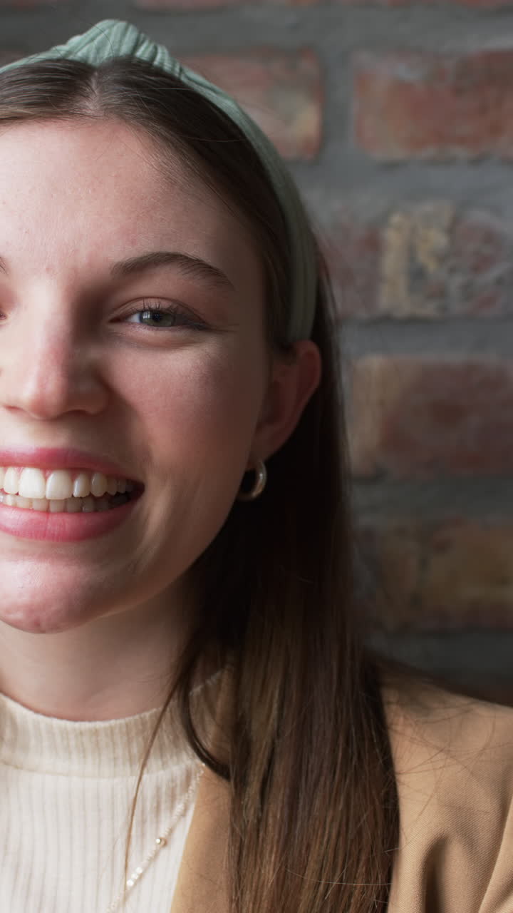 Vertical video: Smiling woman in business attire posing against brick wall background