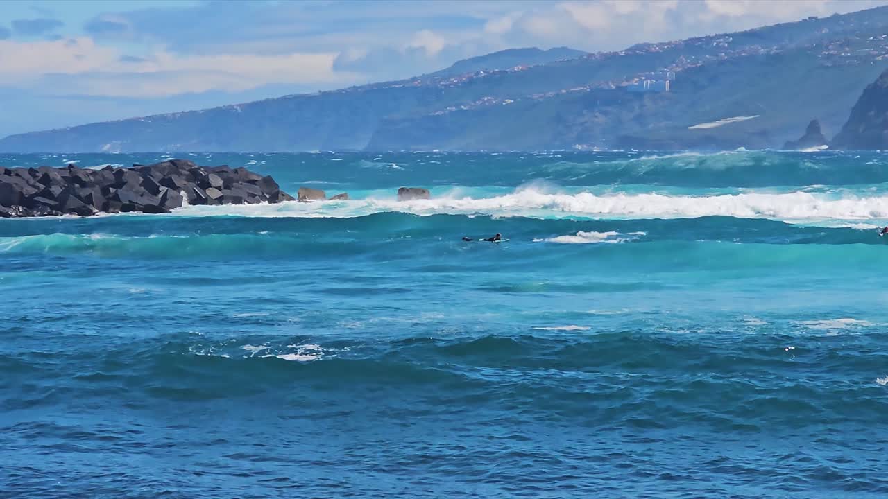 Surfer riding a wave at Puerto, Spain with clear blue waters and rocky coastline