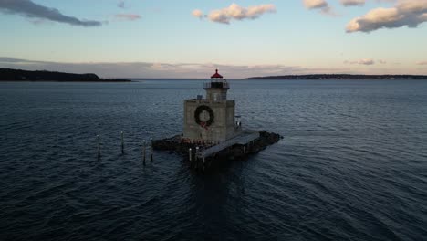 An-aerial-view-of-the-Huntington-Harbor-Lighthouse-on-Long-Island,-NY-at-sunset,-with-a-Christmas-wreath