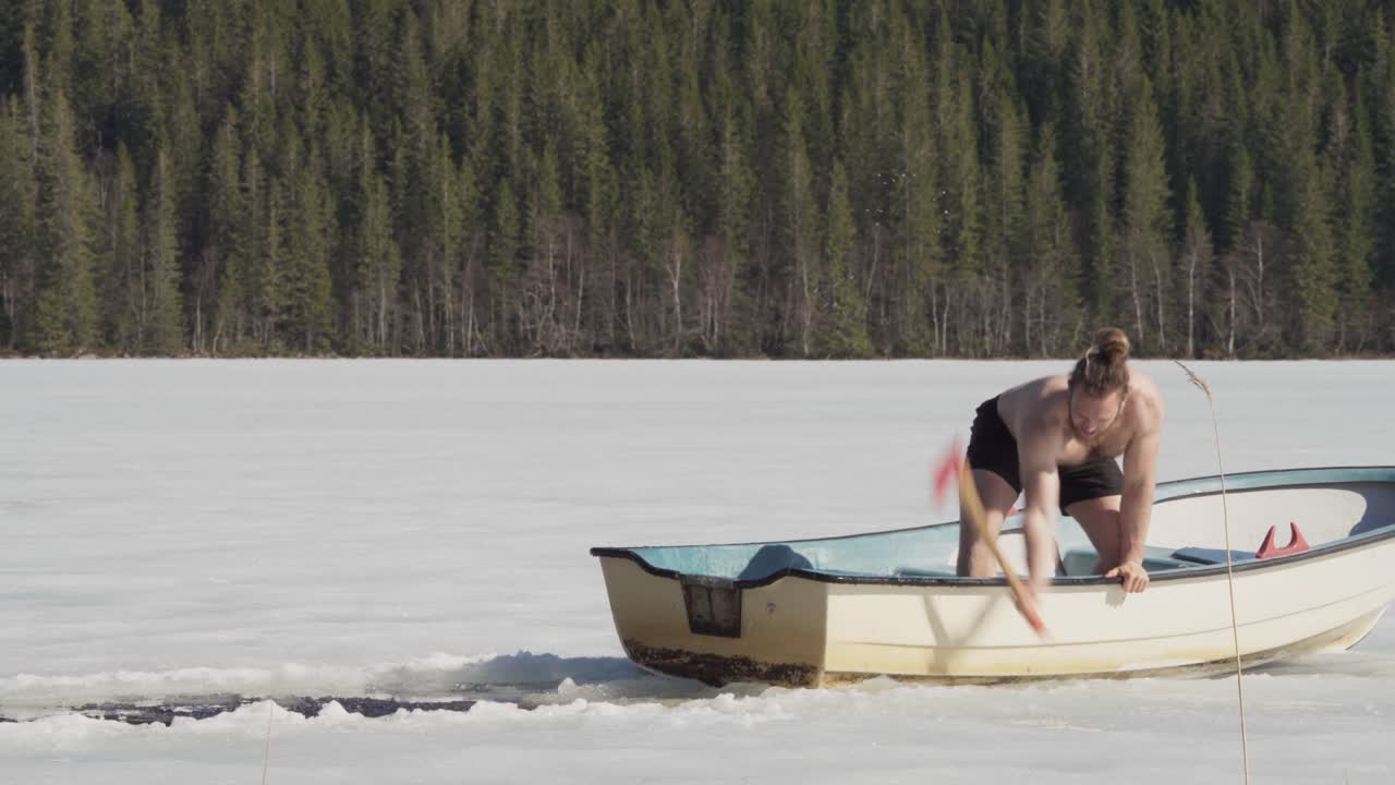 hombre en un bote de remo rompiendo hielo usando un hacha en un lago helado durante el invierno
