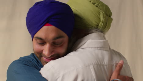 close up studio shot of adult sikh son embracing senior father both wearing turbans against plain background 1