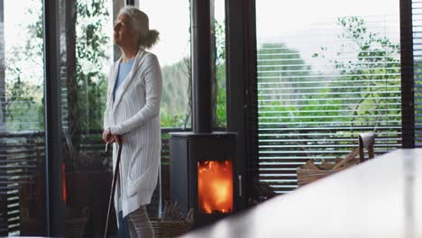 Senior-mixed-race-woman-leaning-on-walking-cane-standing-next-to-fireplace