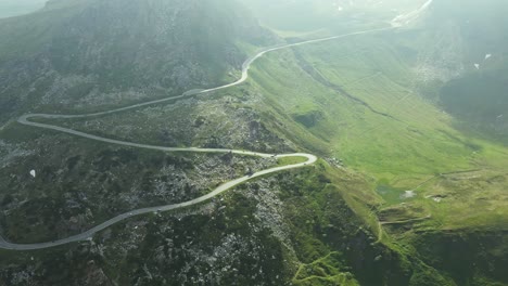 an aerial video captures a winding mountain road snaking through a rugged green landscape. the curves of the road contrast beautifully with the rocky terrain and rolling hills, bathed in soft sunlight