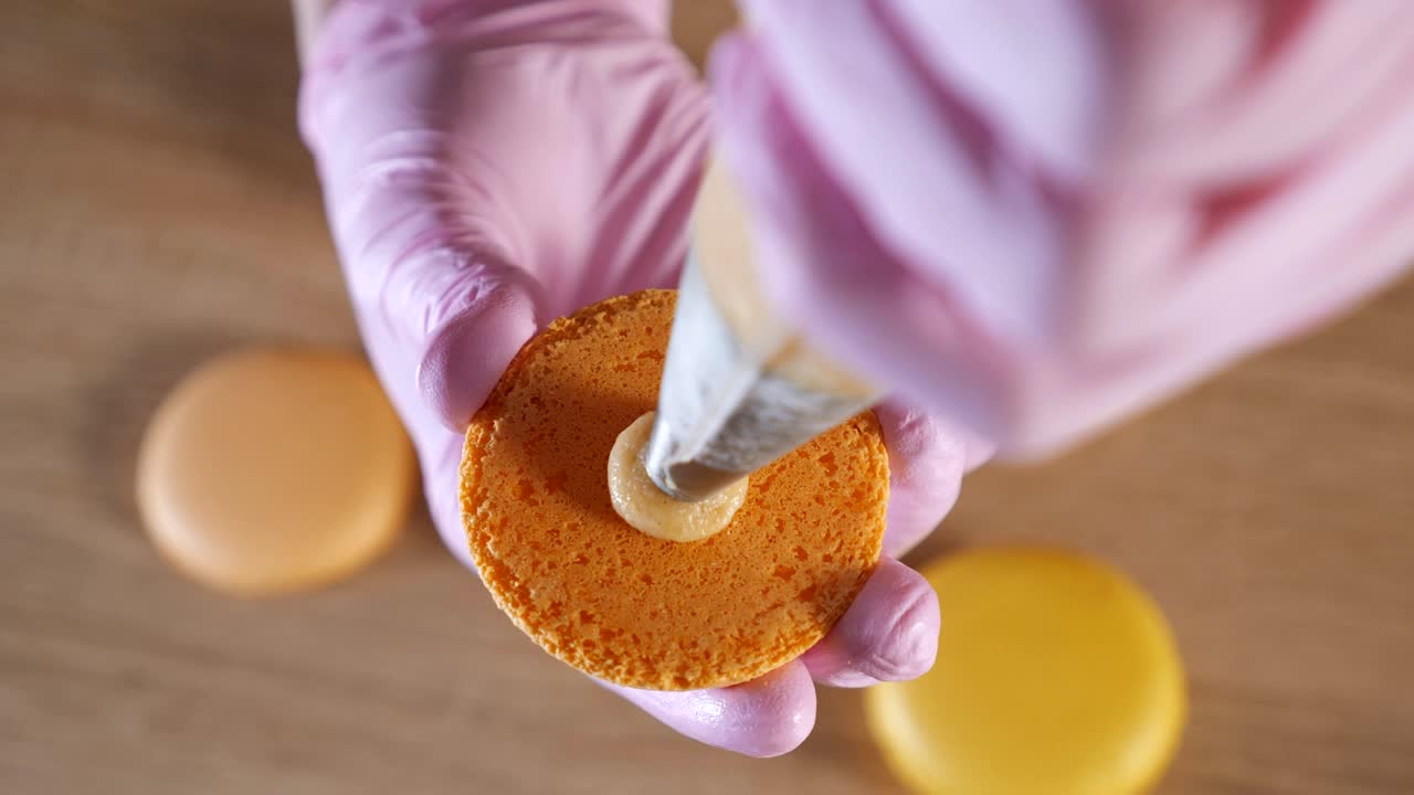 페이스트리 셰프는 레몬 마카룬을 크림으로 채우고 있습니다. 과자 가방을 사용해서요.