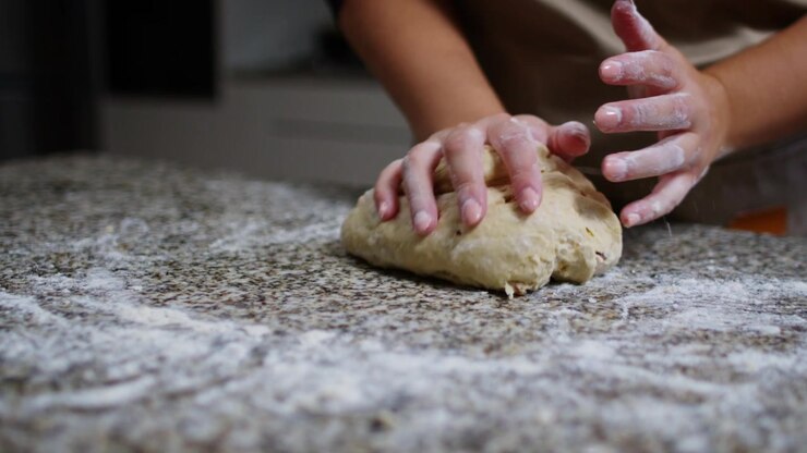 A close-up slow-motion shot of hands kneading dough with slight camera movement, focusing on the texture and motion of the dough, set on a flour-dusted countertop.