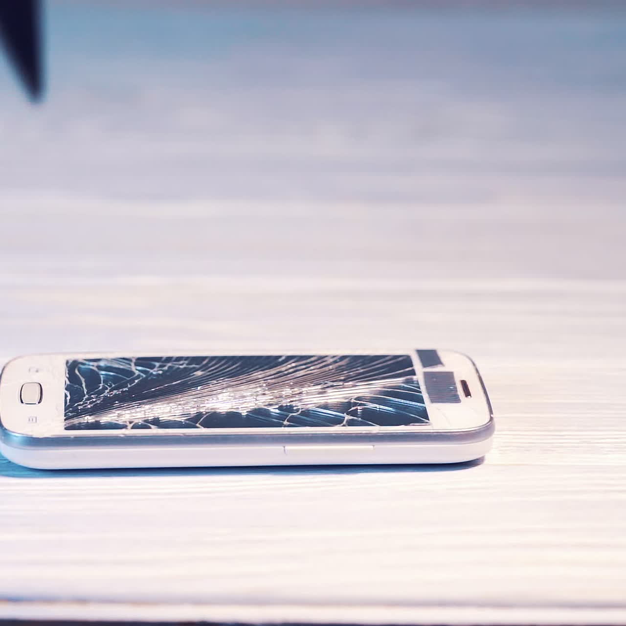 Hammer smashes smartphone and the screen shatters into pieces. Modern cellphone is broken by a hammer. Camera close up.