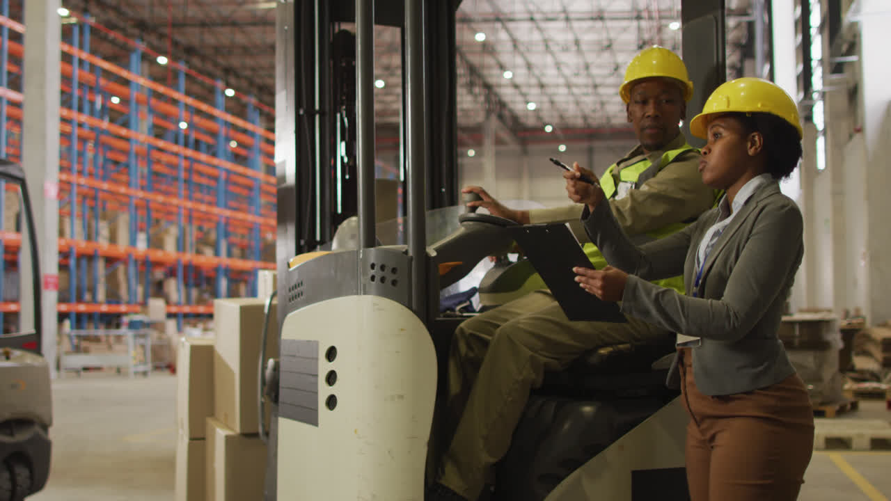 African american male and female workers wearing safety suits and talking in warehouse