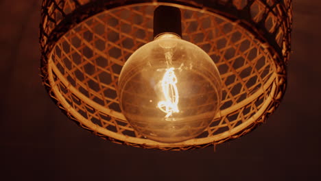 close-up footage of a glowing light bulb inside a woven wicker lampshade. the warm ambient glow creates a cozy atmosphere, highlighting texture and detail in a rustic, handcrafted interior design