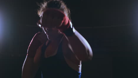 looking into the camera a beautiful female boxer strikes against a dark background with a backlit light. steadicam shot