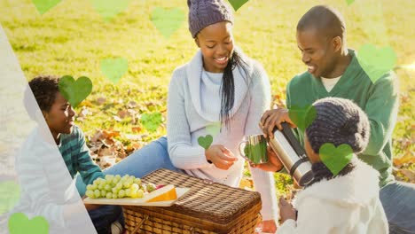 Animation-Von-Grünen-Herzen-über-Einem-Picknickkorb-Und-Einer-Afroamerikanischen-Familie-Im-Park