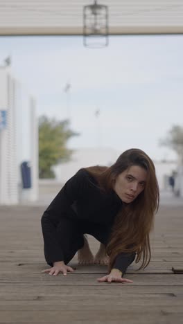 woman in black crouching on a wooden boardwalk