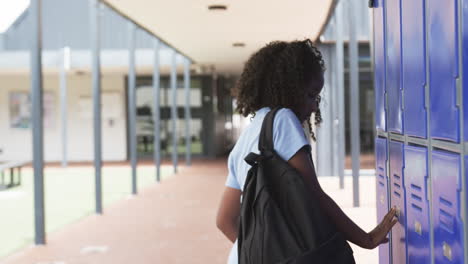 biracial girl with curly hair at school lockers, holding a red book