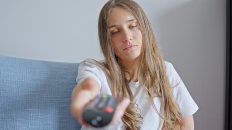 mujer sostiene el control remoto de cerca disparó cambiando los canales de televisión en casa sola sentada en el sofá en la sala de estar