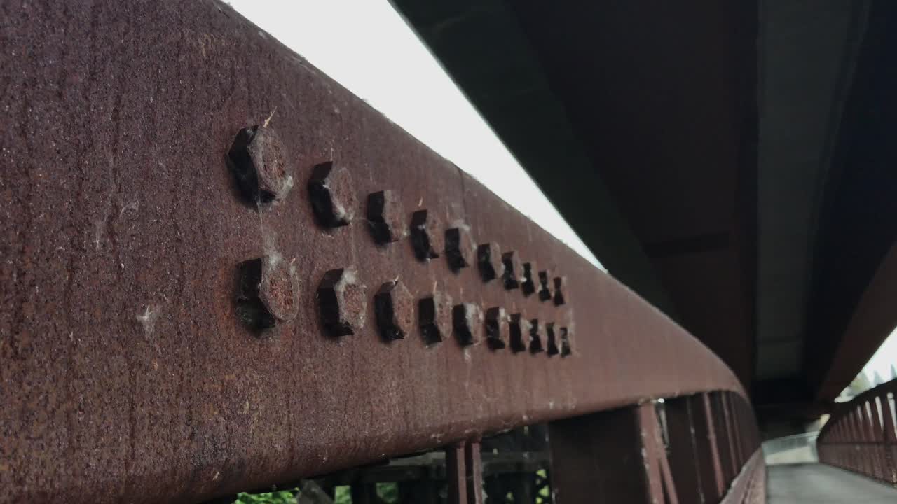 una toma de mano de los pernos oxidados en un viejo puente peatonal de metal sobre un río