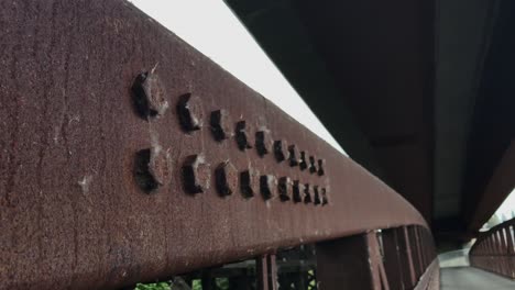 A-handheld-shot-of-the-rusted-bolts-on-an-old-metal-footbridge-over-a-river