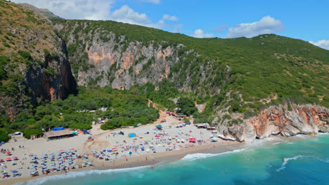 Aerial-drone-rotating-shot-flying-over-Gjipe-beach-with-impressive-canyon-and-mountains-in-the-background-on-a-cloudy-day