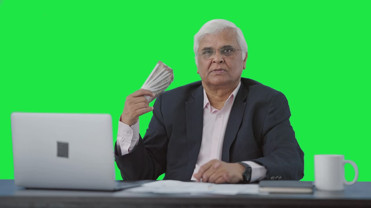 Confident Indian senior businessman using money as fan Green screen